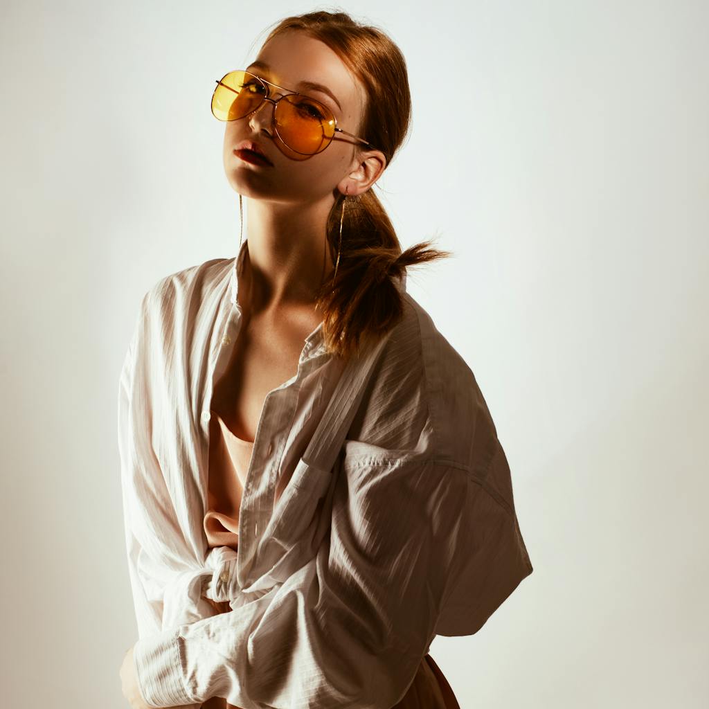 Trendy woman posing in oversized shirt and sunglasses, exuding modern fashion style.